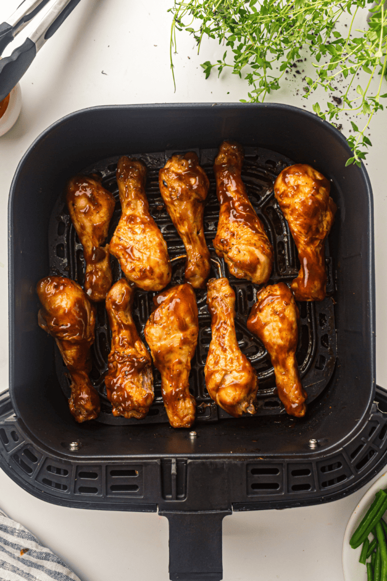 BBQ-coated chicken drumsticks in a mixing bowl, ready to return to the air fryer for a final caramelized finish.