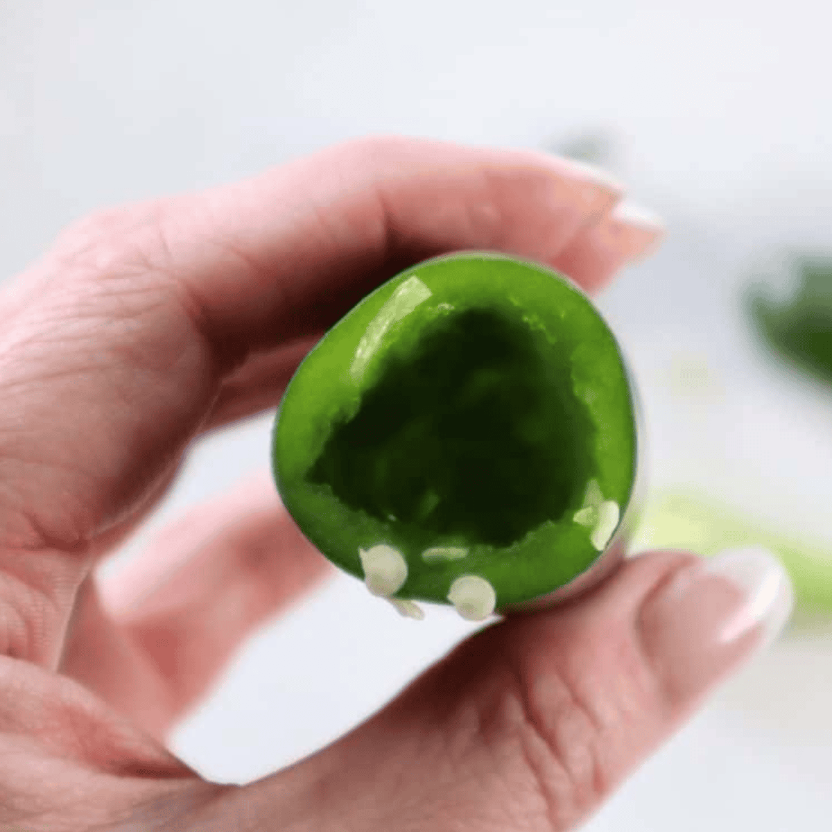 Sliced jalapeños with tops removed and seeds being scooped out to reduce heat.
