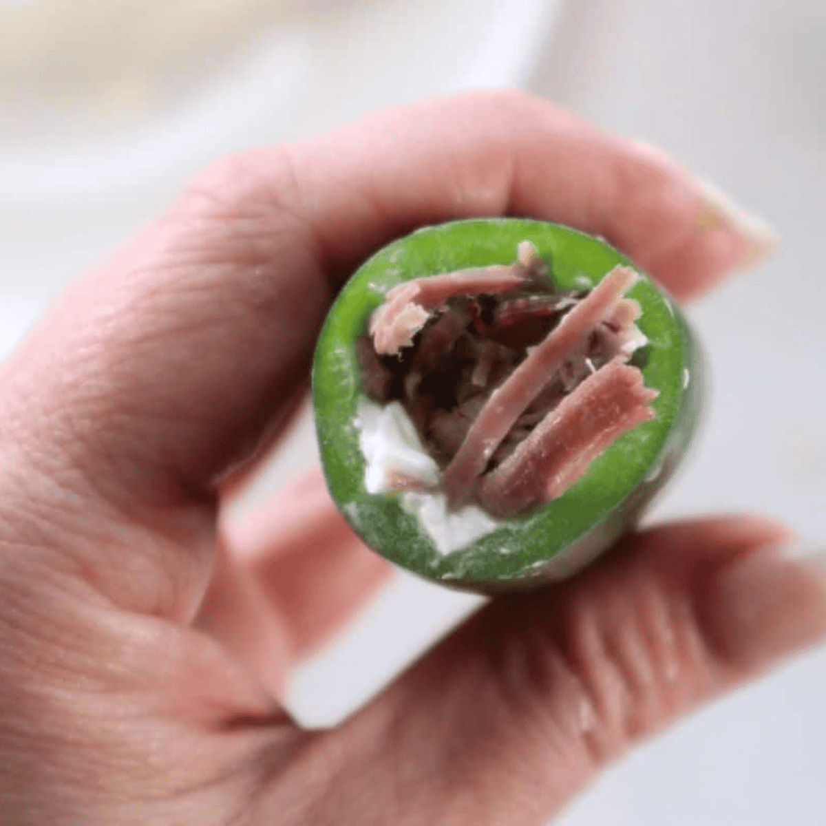 Jalapeño halves being stuffed with cream cheese and shredded brisket filling.