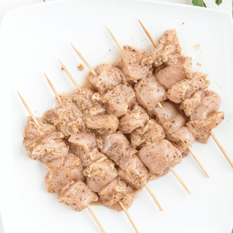Marinated chicken cubes threaded onto soaked wooden skewers, spaced evenly for cooking.