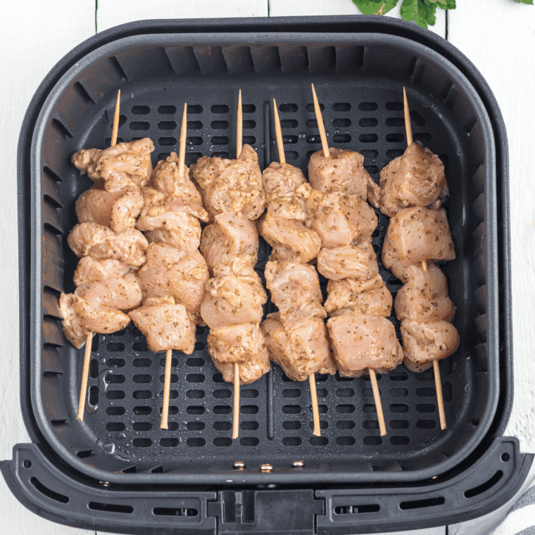 Chicken skewers in the air fryer basket, golden brown, being flipped halfway through cooking.