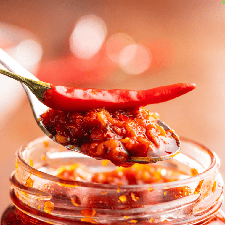 A jar of homemade chili garlic sauce with fresh red chilies and garlic, resembling Huy Fong’s classic version.