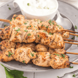 Air Fryer Greek Chicken Kebabs on a white plate with a side of creamy tzatziki sauce