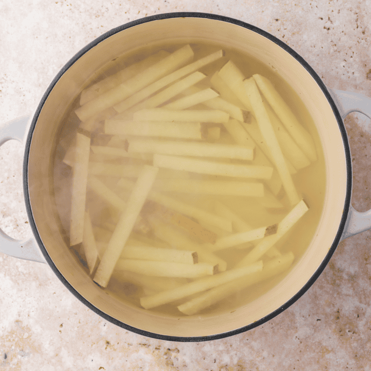 Boiling jicama fries for 10-12 minutes until tender, preparing them for crisping in the air fryer.