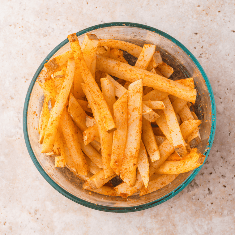 Draining jicama fries and coating them with olive oil, sweet paprika, garlic powder, and salt for even seasoning.