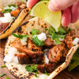 Air fryer pork carnitas tacos on corn tortillas topped with diced white onion, cilantro, and a lime wedge