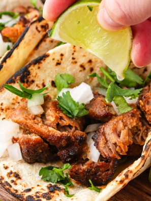 Air fryer pork carnitas tacos on corn tortillas topped with diced white onion, cilantro, and a lime wedge
