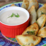 Air fryer spinach and cheese empanadas on a white plate with a bowl of sour cream dip