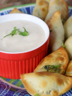 Air fryer spinach and cheese empanadas on a white plate with a bowl of sour cream dip