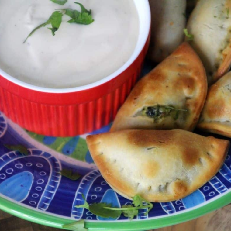Platter of air fryer spinach and cheese empanadas with a bowl of sour cream dip in the center