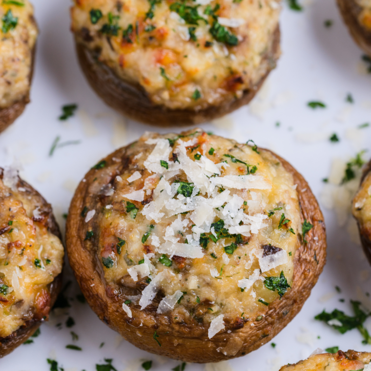 Close-up of golden-brown Air Fryer Stuffed Mushrooms filled with a creamy spinach and parmesan mixture, served on a white plate, showcasing the crispy tops and tender mushroom caps.