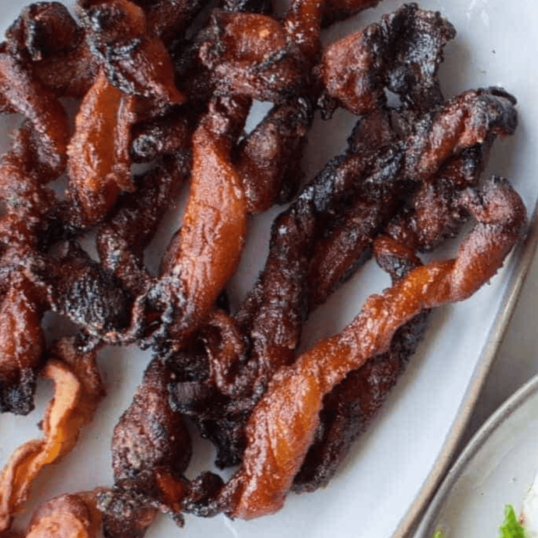 A plate of crispy Air Fryer Twisted Candied Bacon drizzled with a sticky glaze, showcasing its delicious caramelized texture and enticing sweetness.