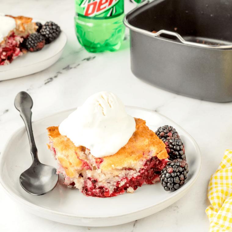 Air fryer blackberry cobbler in a round pan with a golden, puffed topping and juicy baked blackberries