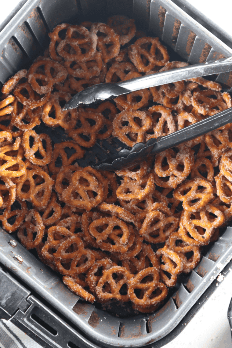 Coated cinnamon sugar pretzels in an air fryer basket with metal tongs on top.