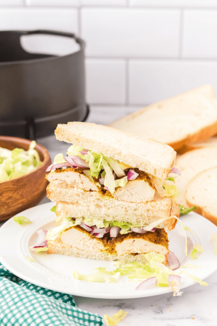 Air fryer curried chicken sandwich with crispy bread, lettuce, and red onion on a plate