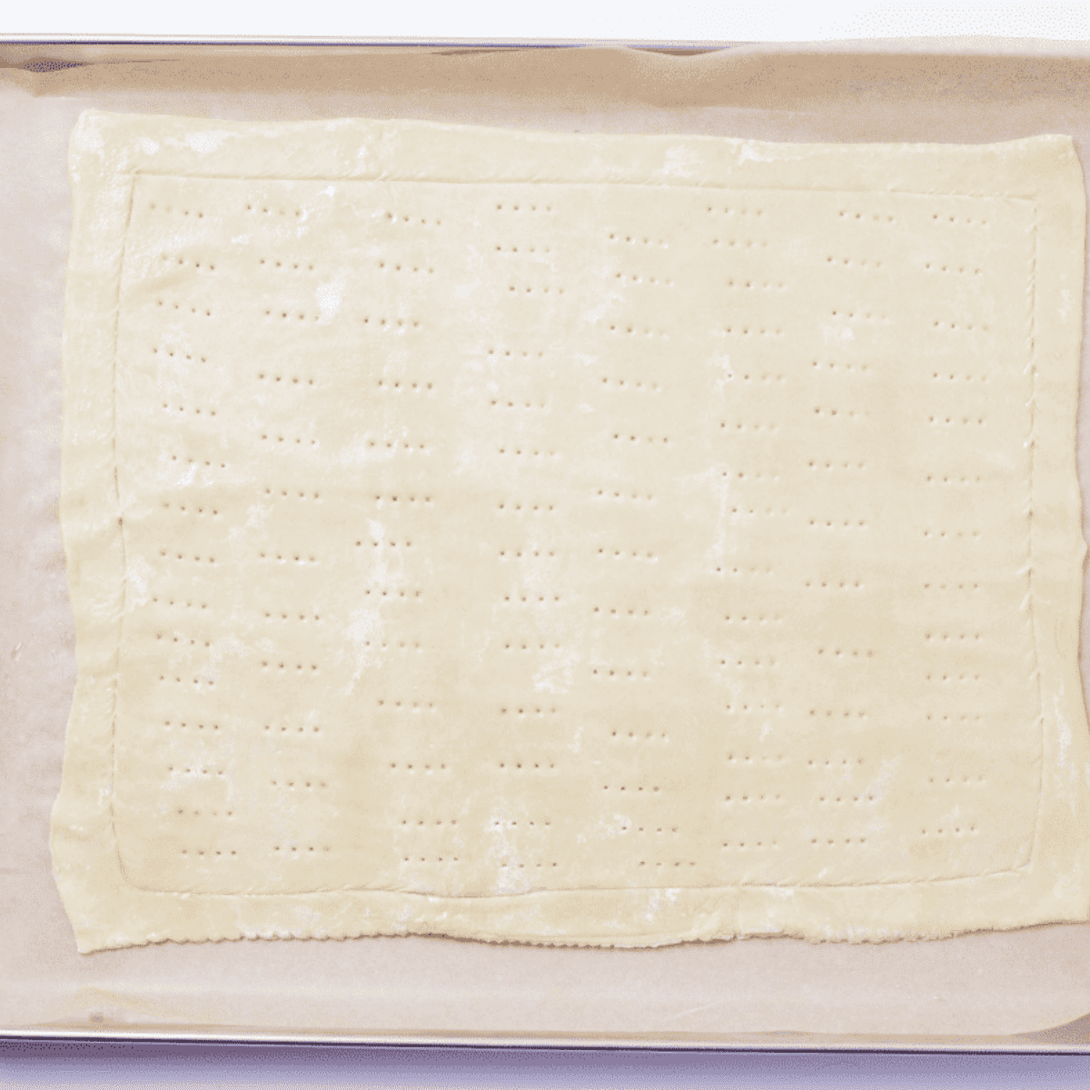 Thawed puff pastry sheet being rolled out on parchment paper, with an air fryer preheating in the background.