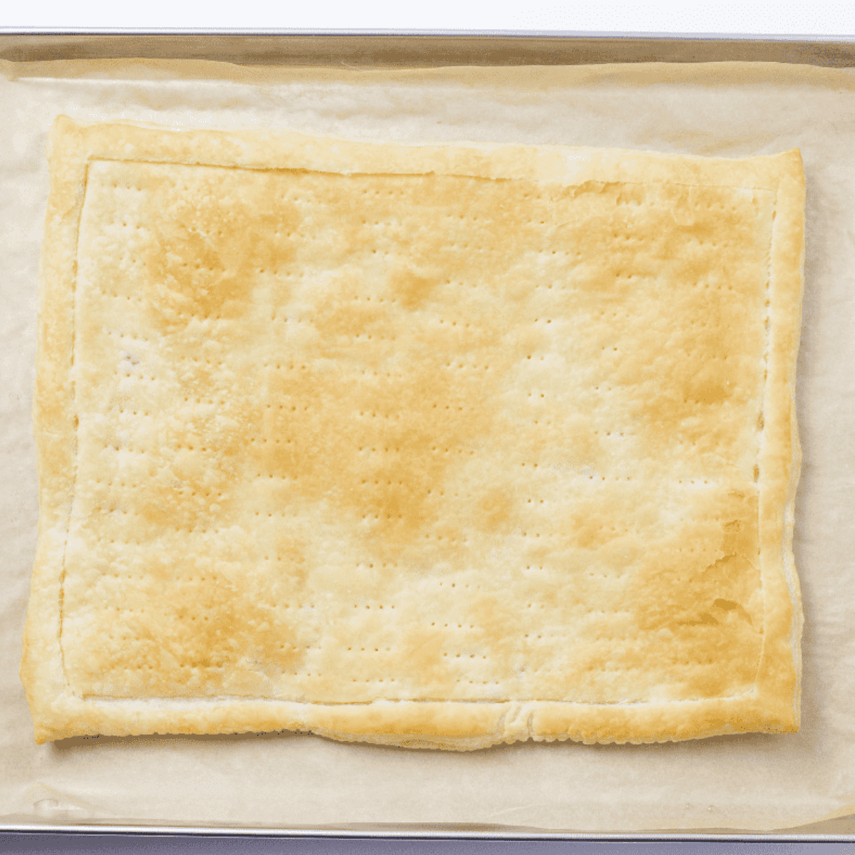 Puff pastry sheet with a scored border and brushed with oil, placed in an air fryer basket ready to cook.
