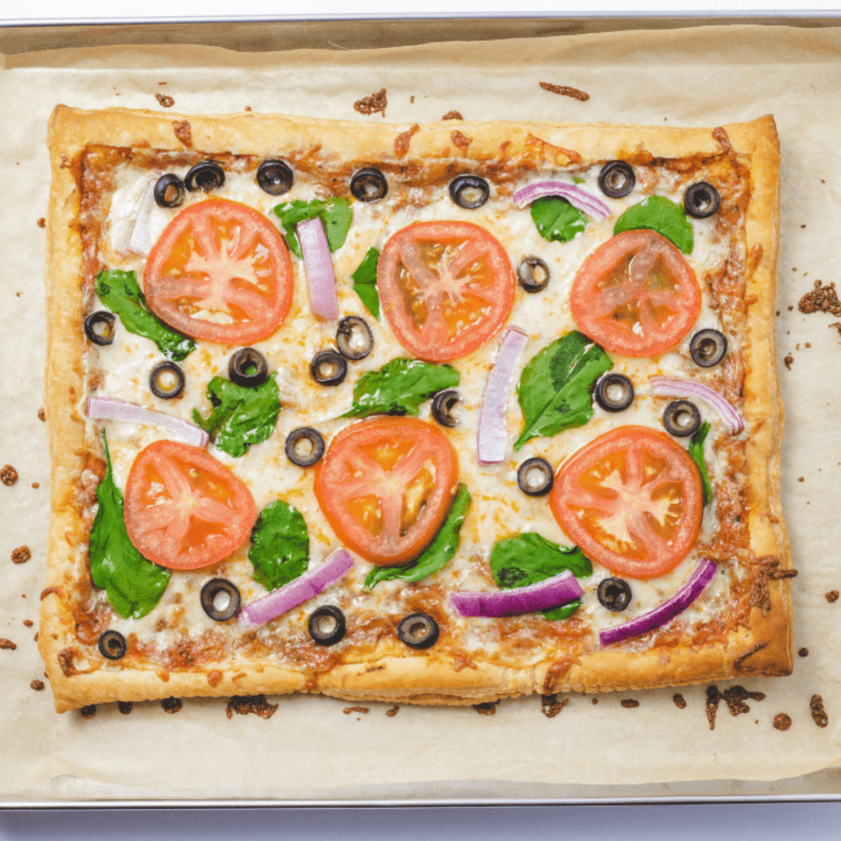 Air fryer puff pastry pizza topped with cheese and vegetables, cooking in the basket with fresh basil ready for garnish.