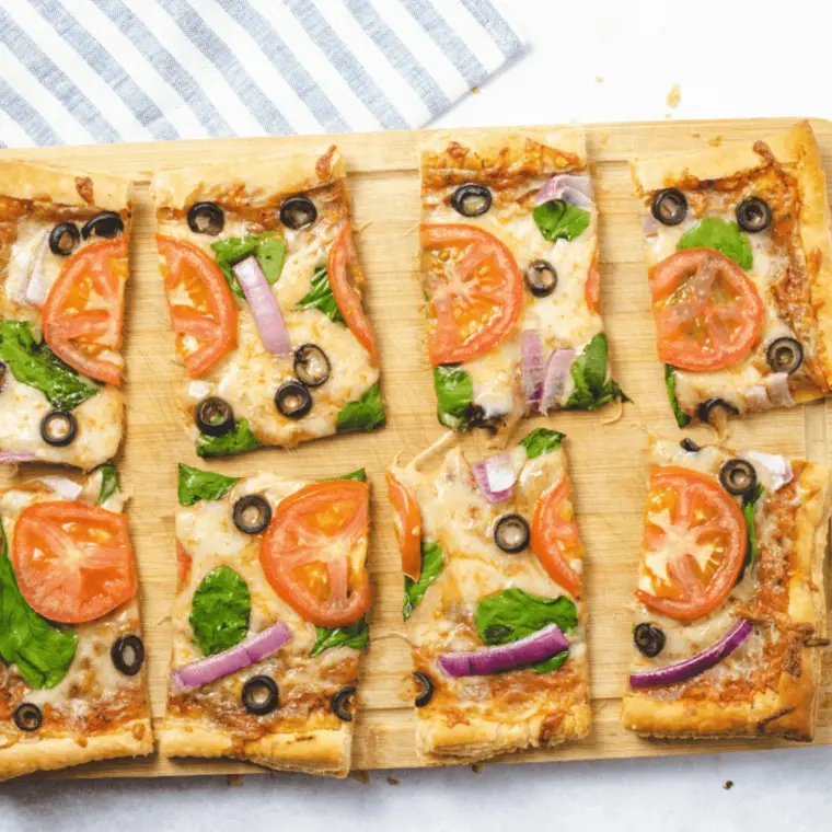 Square of air fryer puff pastry pizza on a wooden board with a crisp golden border