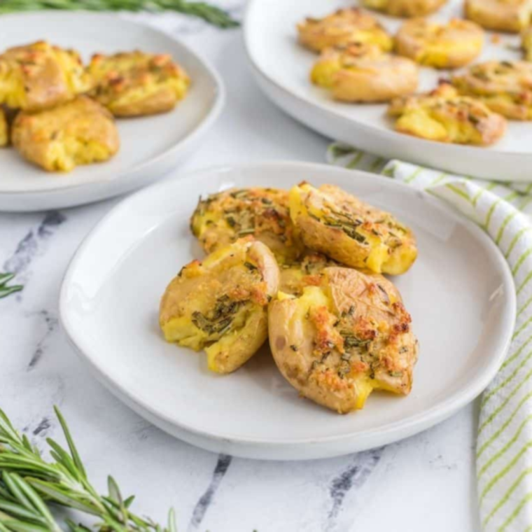 Air Fryer Rosemary Garlic Smashed Potatoes topped with fresh rosemary and garlic, served on a white plate.