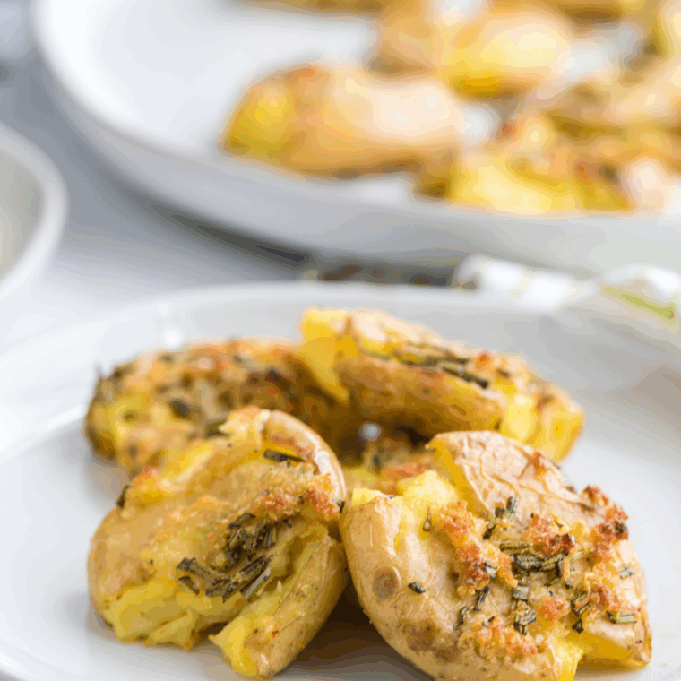Golden, crispy fried smashed potatoes served on a plate, garnished with fresh herbs.