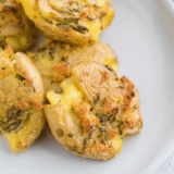 Golden, crispy fried smashed potatoes served on a plate, garnished with herbs.