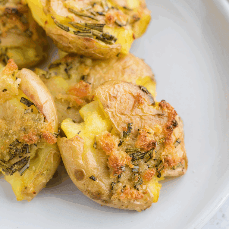 Golden, crispy fried smashed potatoes served on a plate, garnished with herbs.