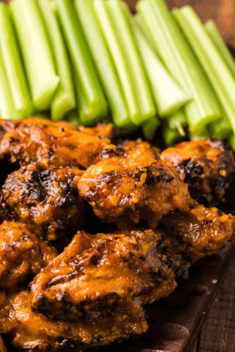 Plate of crispy Wingstop copycat mango habanero wings coated in a vibrant sweet and spicy sauce, garnished with celery sticks and dipping sauces.