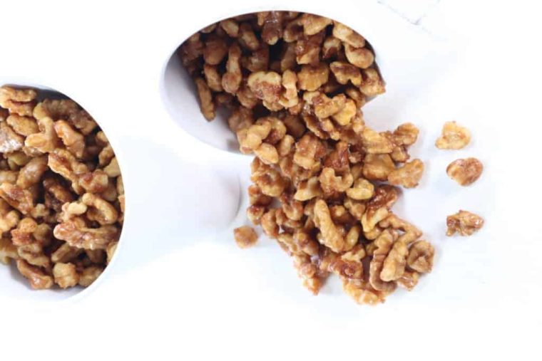 closeup: two small white bowls of air fryer candied walnuts with nuts spilling out of the bowl on the right