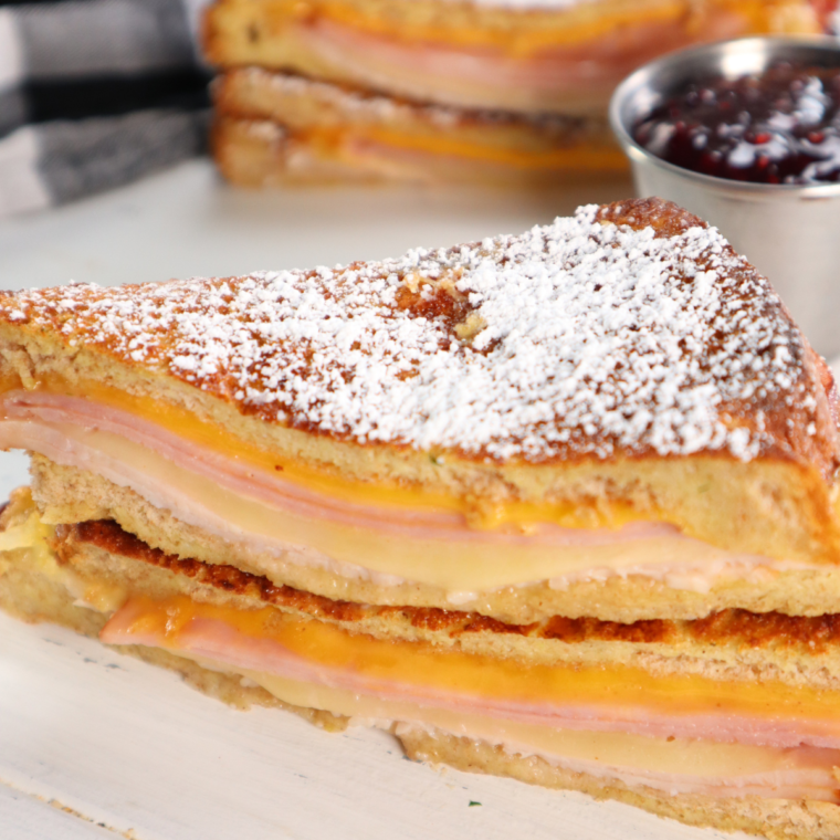 "Air Fryer Monte Cristo Sandwich: A golden-brown, crispy sandwich filled with layers of ham, turkey, and gooey melted cheese, dusted with powdered sugar, and served with a side of raspberry jam."