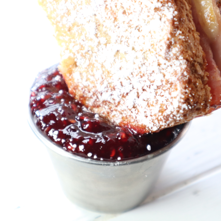 "Close-up of Air Fryer Monte Cristo Sandwich: Crispy, golden-brown sandwich with a gooey cheese and savory ham and turkey filling, garnished with powdered sugar, served on a plate with raspberry jam for dipping."