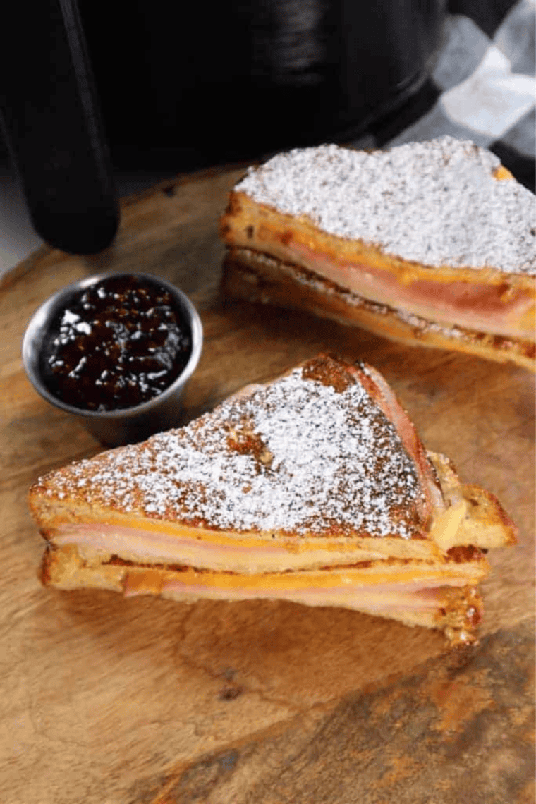 Golden crispy air fryer Monte Cristo sandwich dusted with powdered sugar, sliced to show ham, turkey, and melted cheese filling.