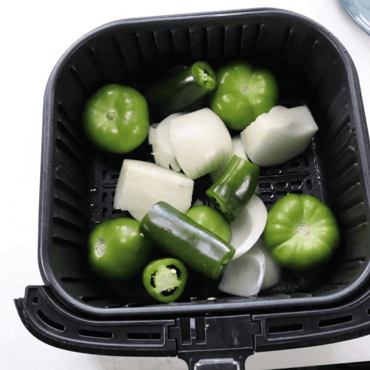 Placing tomatillos, jalapeños, and onion in the air fryer at 390°F for 5 minutes to roast.