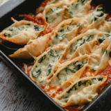 Air fryer stuffed spinach pasta shells on a white plate, filled with ricotta and spinach and topped with melted mozzarella and marinara