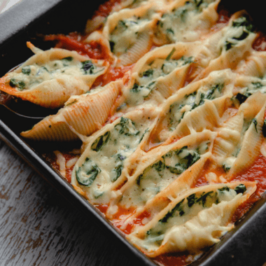 Air fryer stuffed spinach pasta shells on a white plate, filled with ricotta and spinach and topped with melted mozzarella and marinara