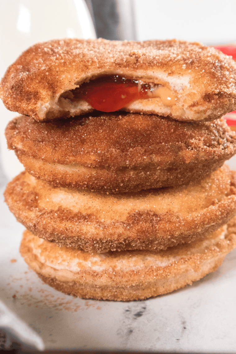 Stack of golden Air Fryer Uncrustable Donuts coated with cinnamon sugar on a white plate