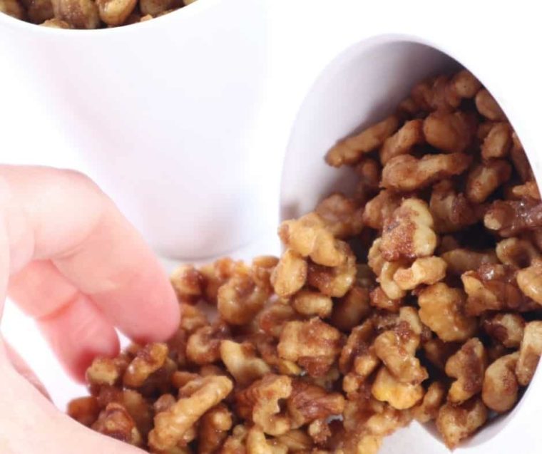 closeup: a hand reaching for some of my candied walnuts air fryer recipe out of a white bowl tipped over