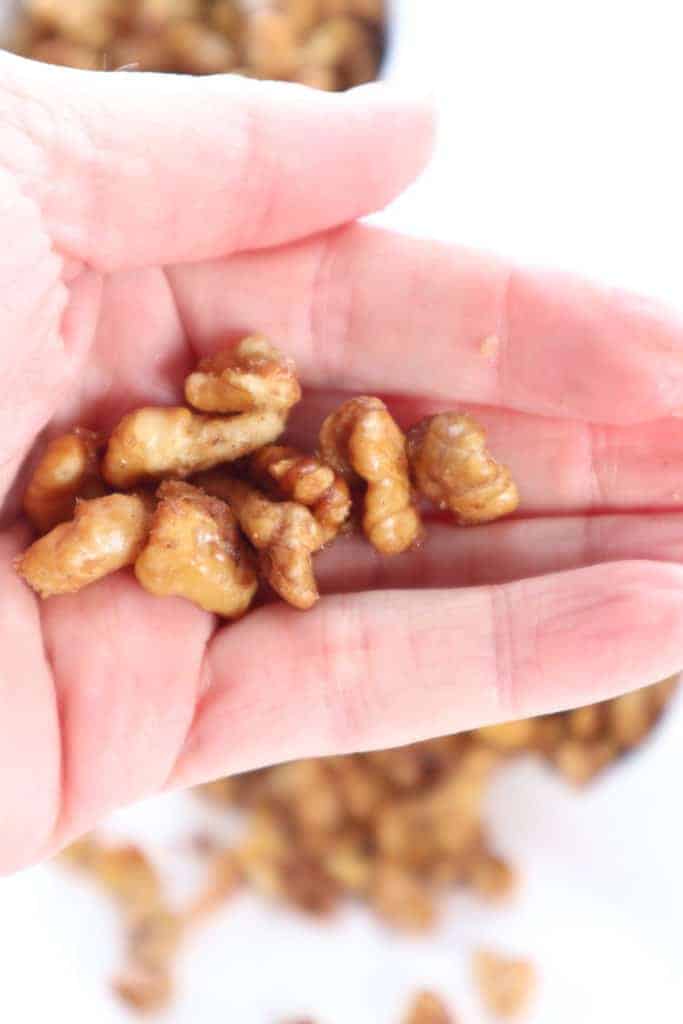 overhead closeup: a hand holding a few candied walnuts made in air fryer 