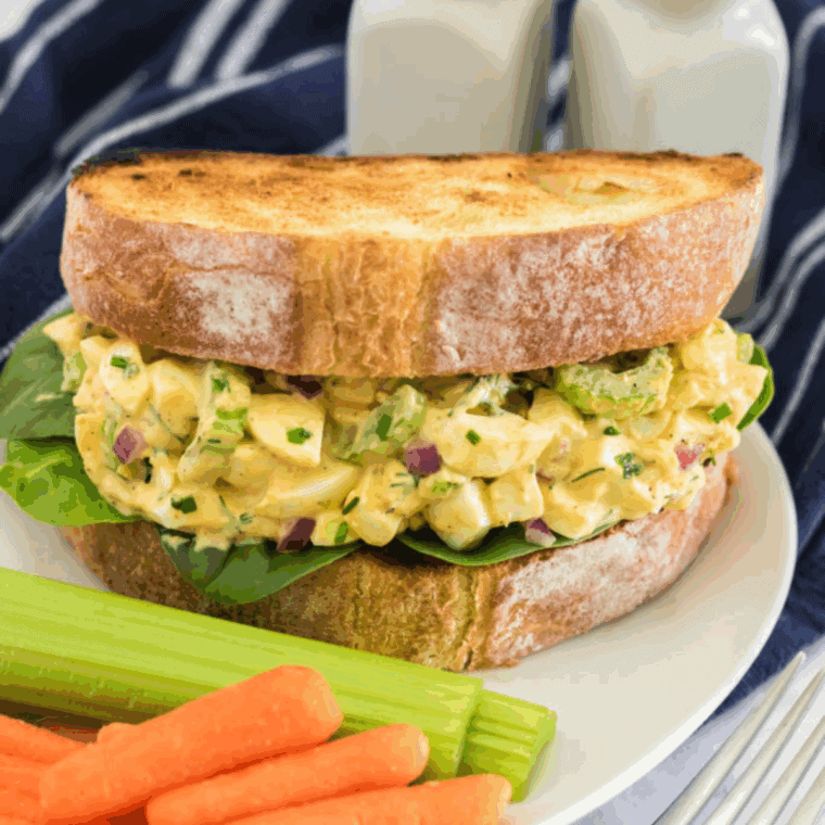 Creamy egg salad with chopped dill pickles served on toasted bread with lettuce, ready for a delicious sandwich or snack.