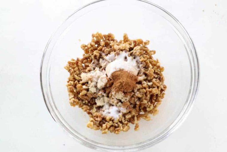 overhead process shot: walnuts tossed in butter with sugar and cinnamon on top in a large glass bowl