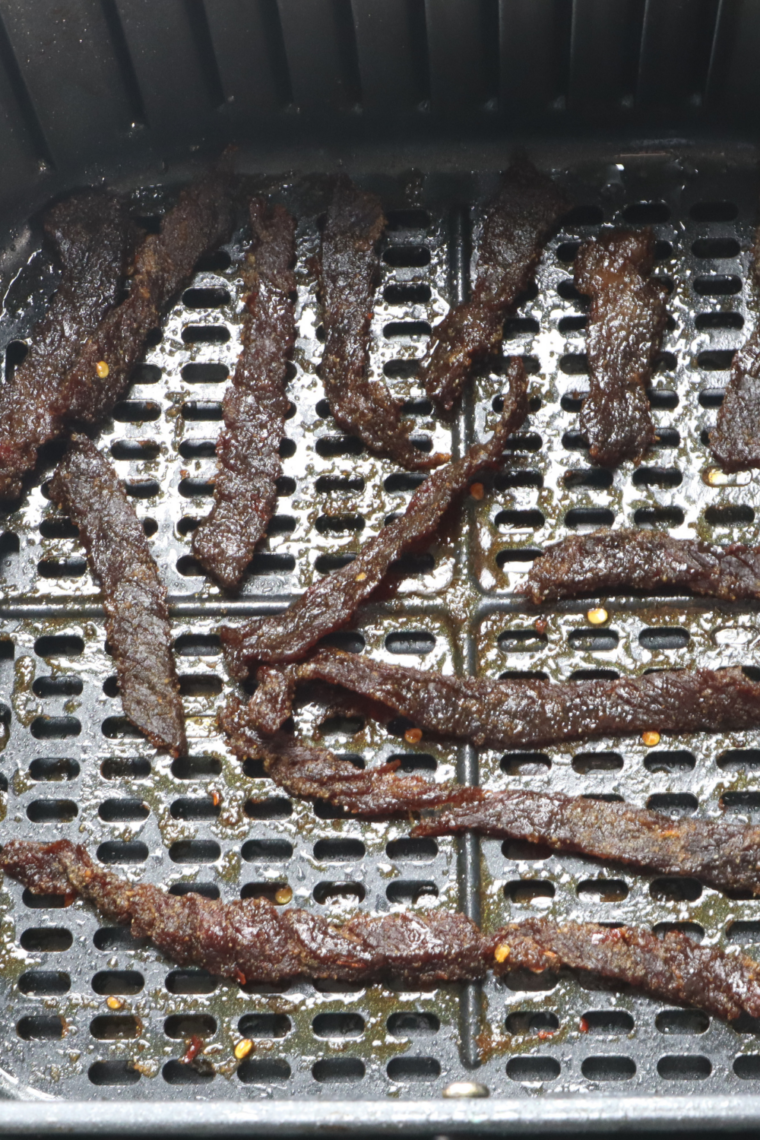 Air fryer beef jerky strips halfway through cooking at 180 degrees, showing darkened color and firming texture