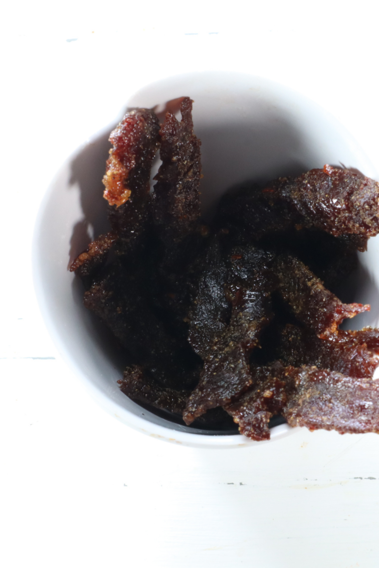 Hand holding a single piece of homemade air fryer beef jerky bent to show its perfect chewy-tender texture