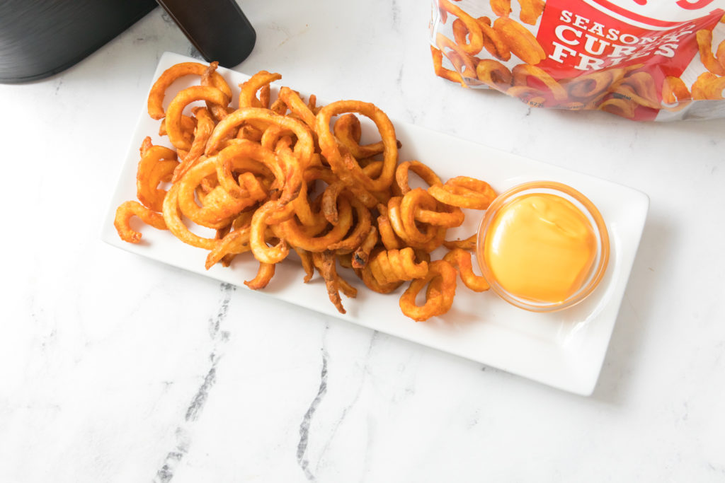 curly fries on a white rectangle plate with yellow dipping sauce