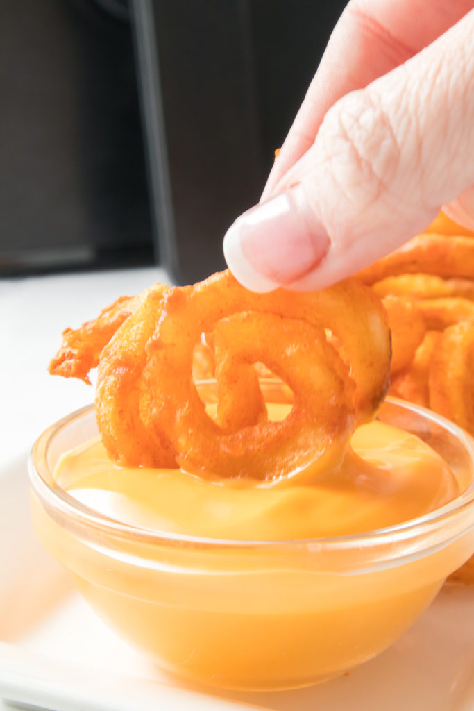 close up of hand dipping curly fries into yellow dipping sauce