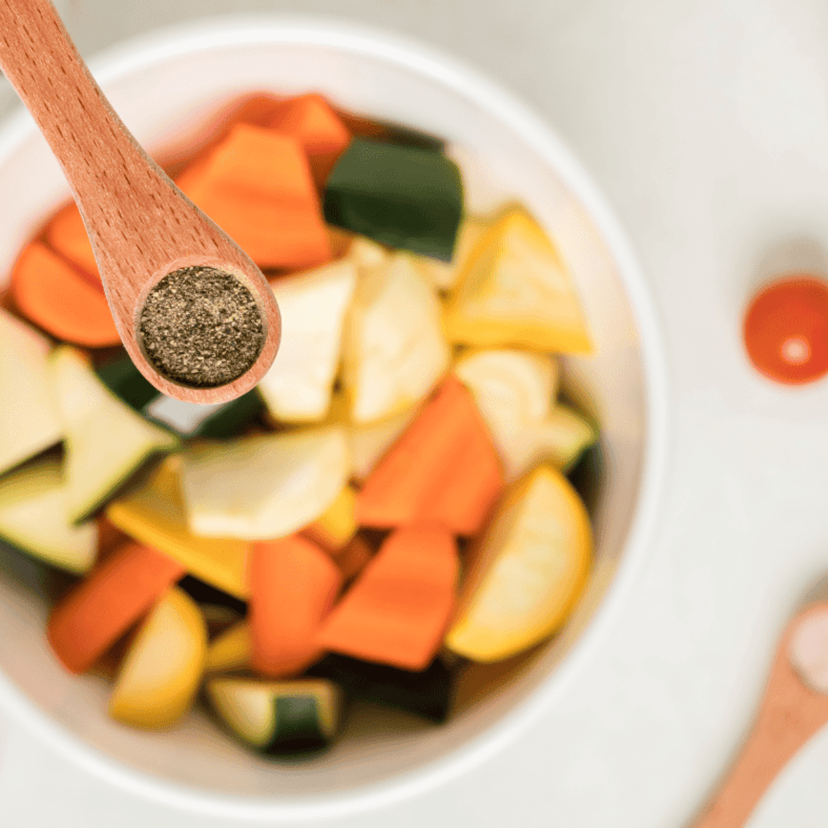 Chopped vegetables in a bowl tossed with olive oil, garlic powder, salt, and pepper.