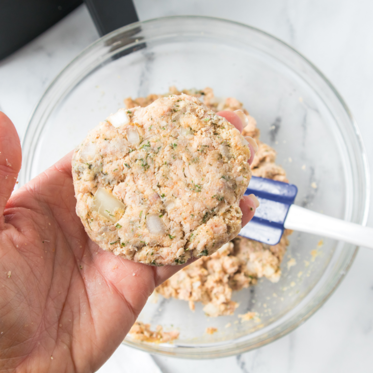 Fresh salmon burger patties chilling on a parchment-lined plate in the refrigerator before cooking