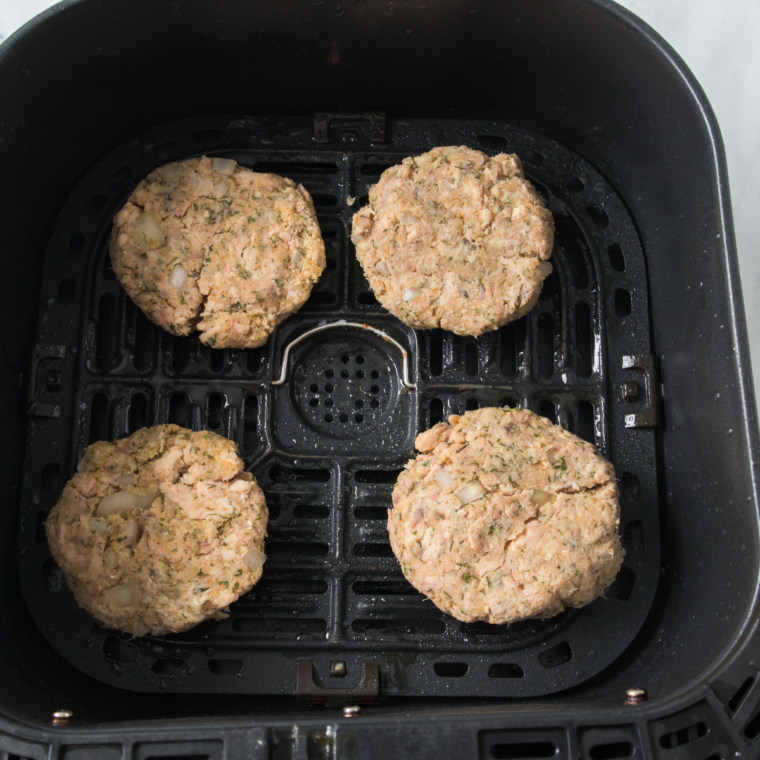 Salmon burgers cooking in air fryer basket until golden brown and crispy on the outside