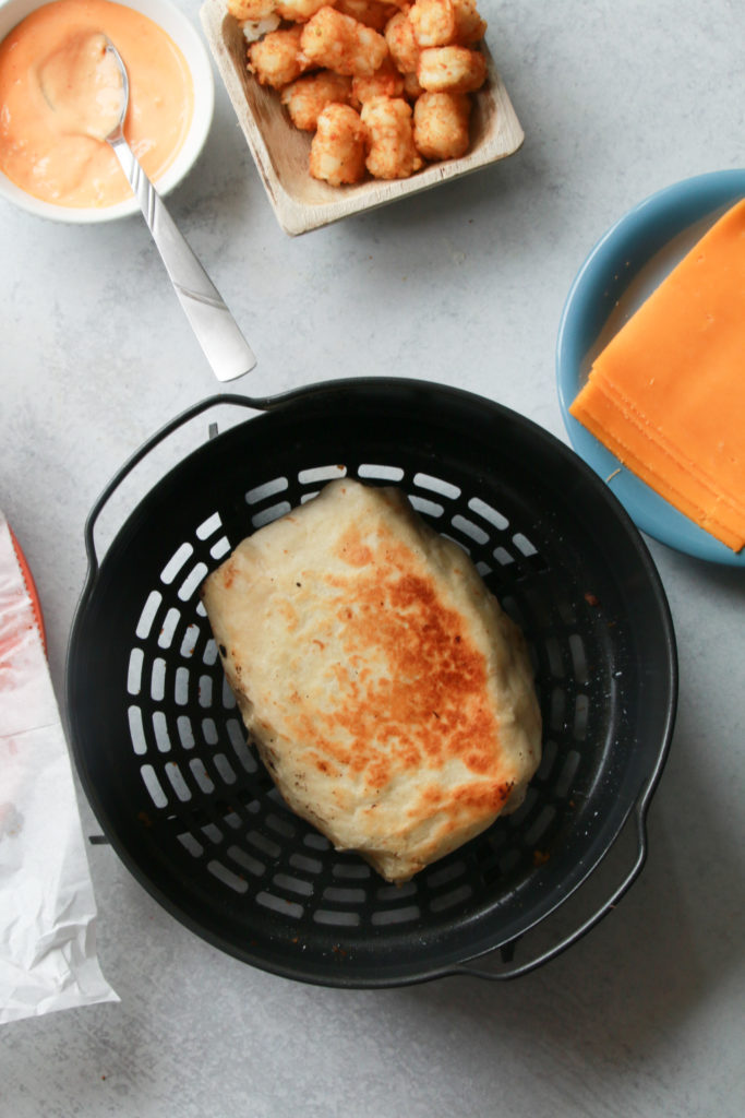 Placing the wrap seam down in an air fryer basket, spraying with olive oil, and air frying for 4-6 minutes at 400°F until golden brown.