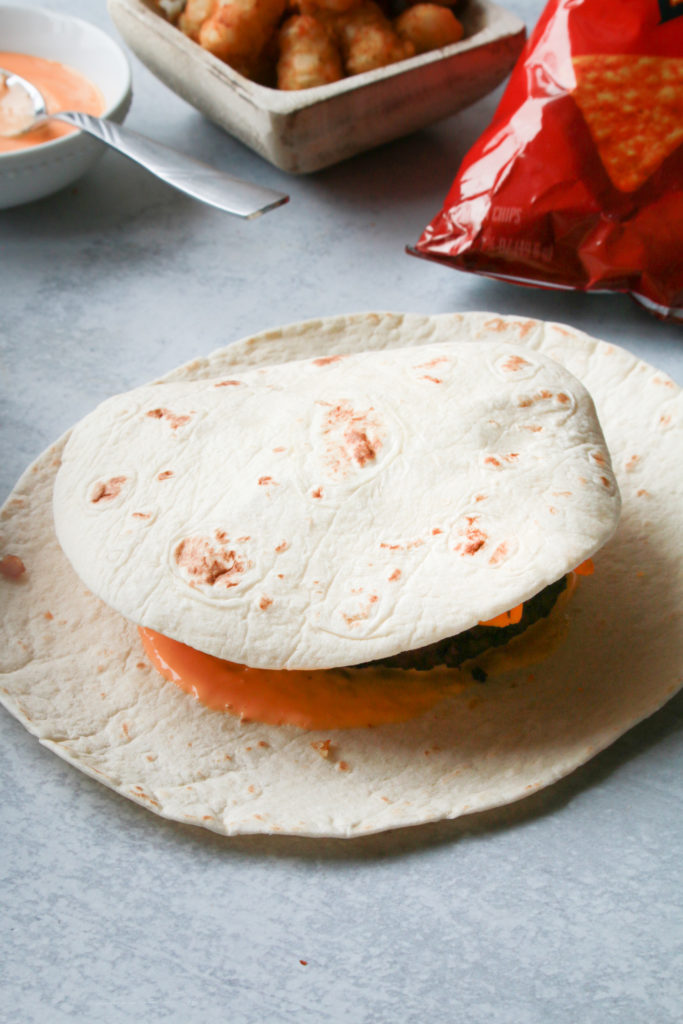 Placing the smaller tortilla on top of the layered ingredients and folding the overhanging corners of the larger tortilla around it.