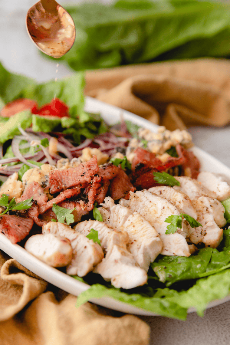 Air fryer Cobb salad with sliced chicken, bacon, hard-boiled egg, avocado, cherry tomatoes, red onion, and blue cheese on a white platter
